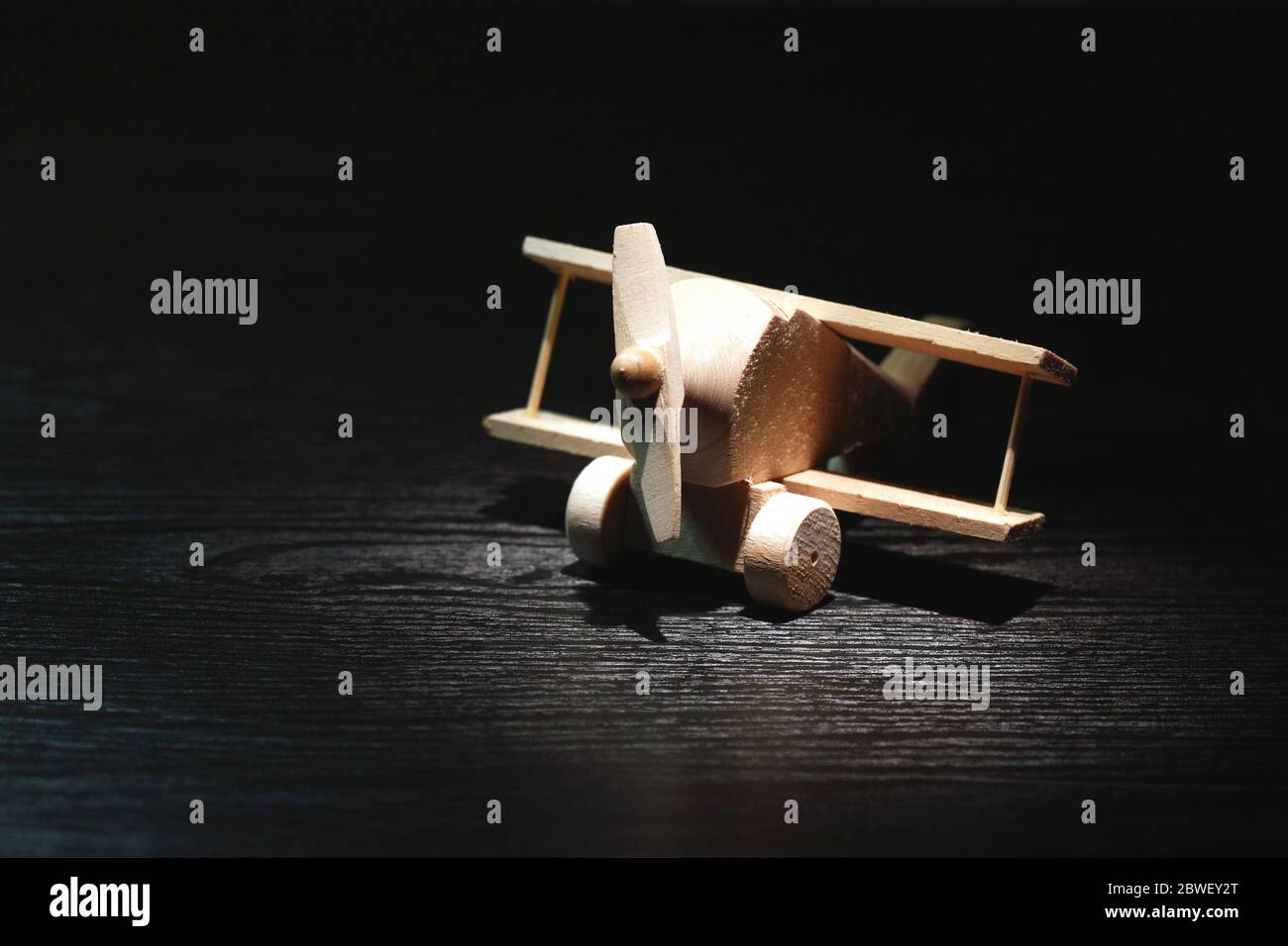 Concetto di viaggio. Piccolo aeroplano di legno sotto il fascio di luce su sfondo scuro Foto Stock