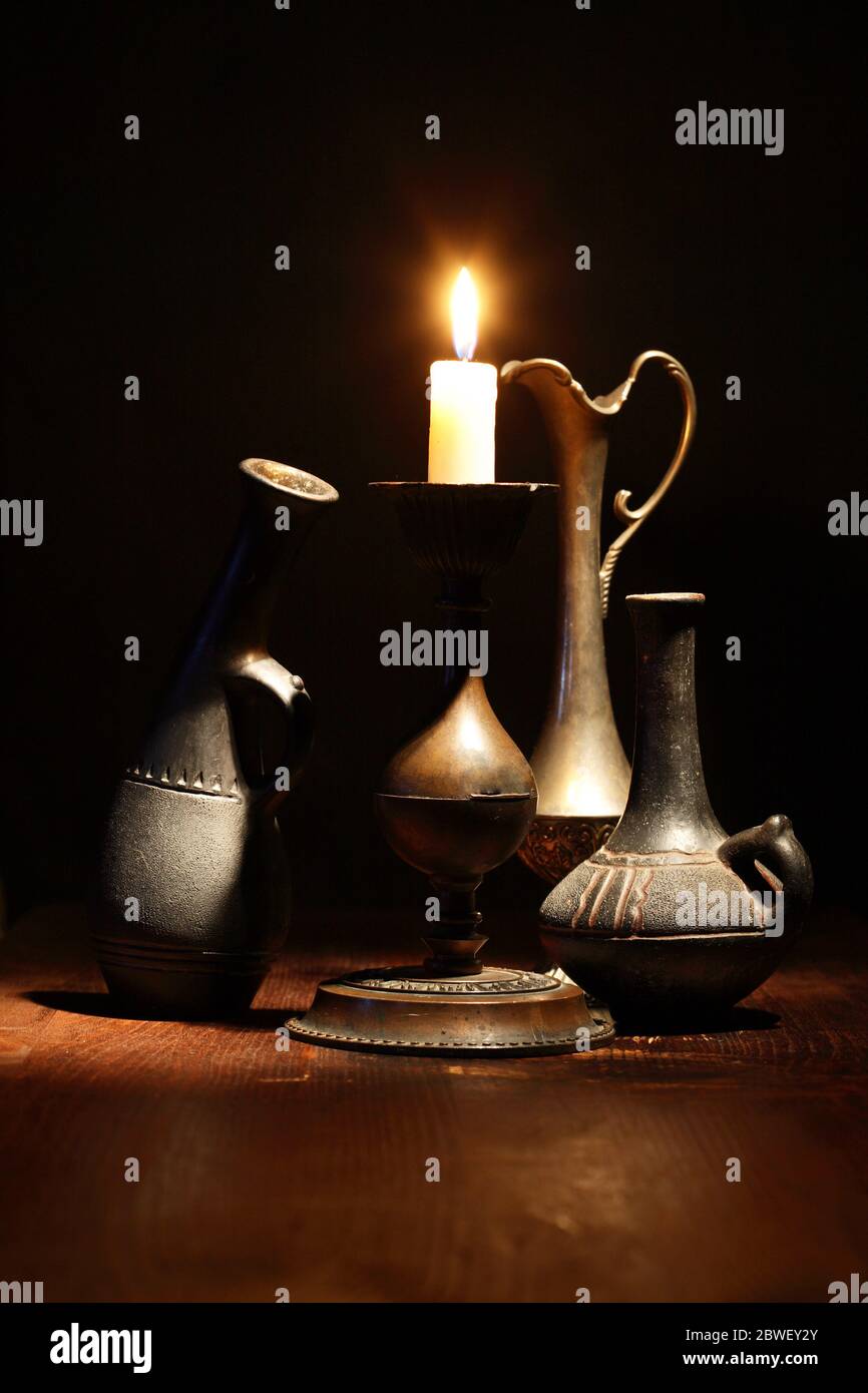 Set di belle antiche vasi vicino luce candela su sfondo scuro Foto Stock