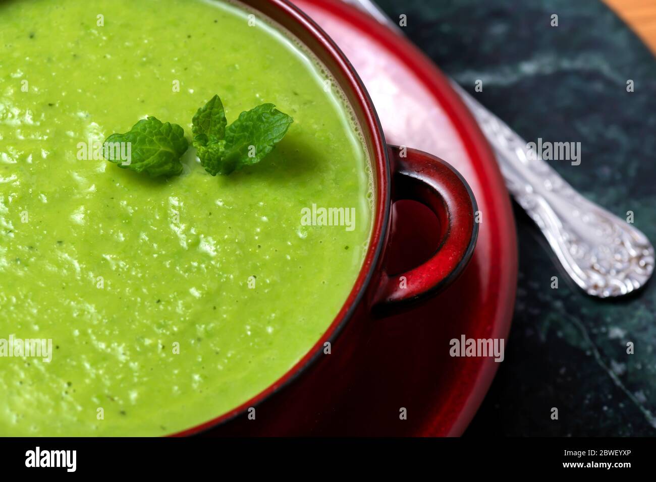 Da sopra ciotola di deliziosa zuppa di piselli vegani a base di piante fatte in casa con foglie di menta fresca servite sul tavolo Foto Stock