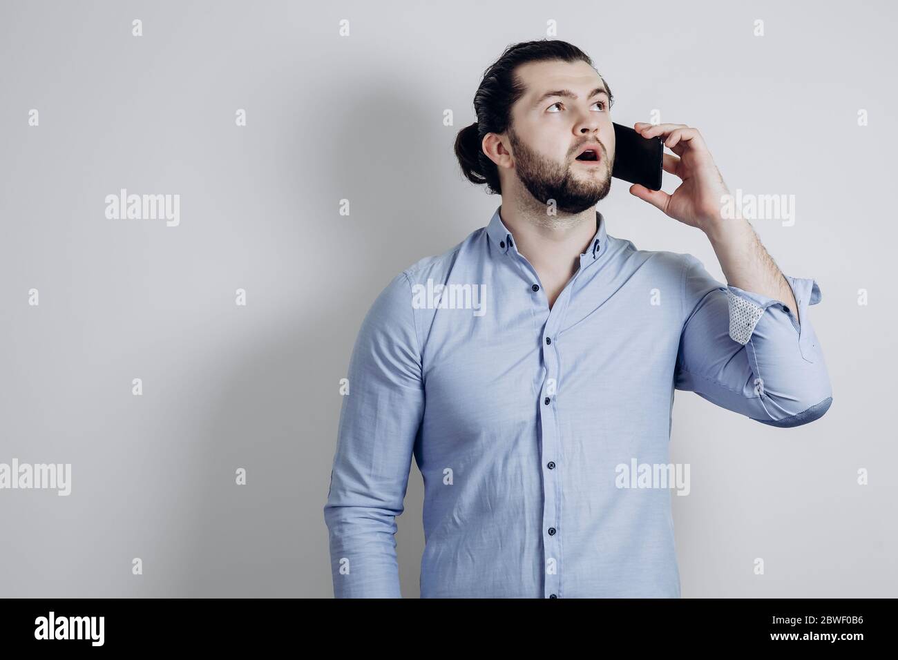 Uomo riuscito con i capelli lunghi sta parlando al telefono ed è sorpreso. Foto Stock