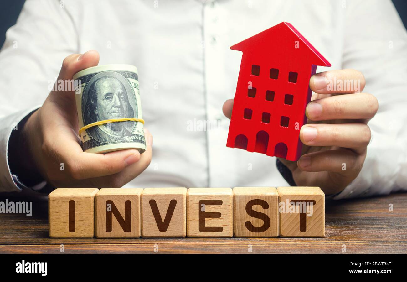Un uomo con dollari e una casa figurina e la parola Invest. Investimenti finanziari immobiliari. Favorevole clima di investimento, alloggi a buon mercato e basso dem Foto Stock