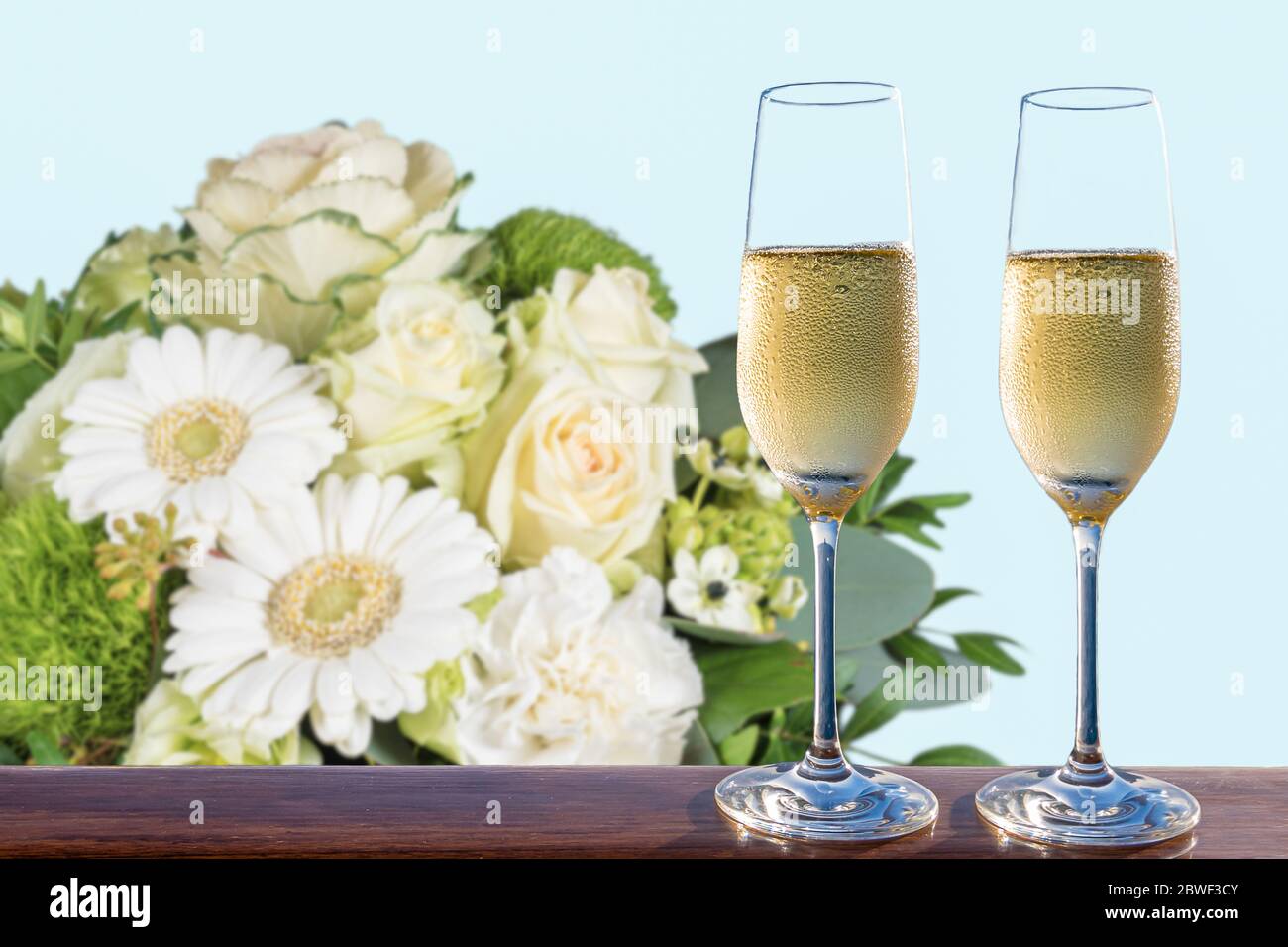 Due bicchieri di champagne e bouquet di fiori bianchi sfocati. Foto Stock