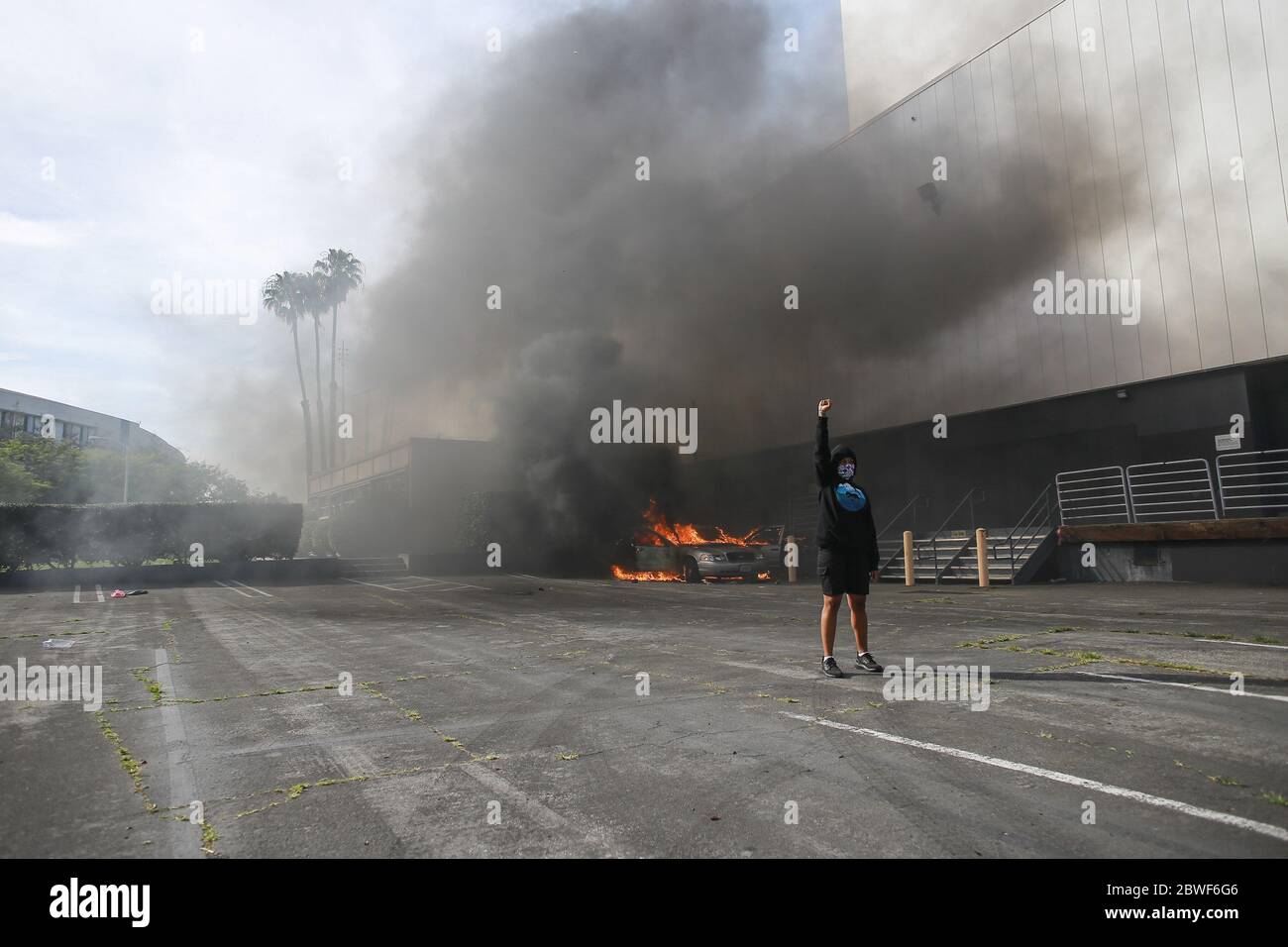 Un manifestante si pone di fronte a un'auto fiammata distrutta da un gruppo di manifestanti durante una protesta contro l'uccisione di George Floyd. I manifestanti scesero per le strade di Los Angeles per il quinto giorno di fila in una posizione contro l'uccisione di George Floyd da parte dell'ex Minneapolis Ufficiale di polizia, Derek Chauvin. Molti manifesti si sono riuniti a Santa Monica, dove una protesta pacifica si è presto devoluta in scontri con la polizia e pesanti saccheggi da parte di molti manifestanti. Foto Stock