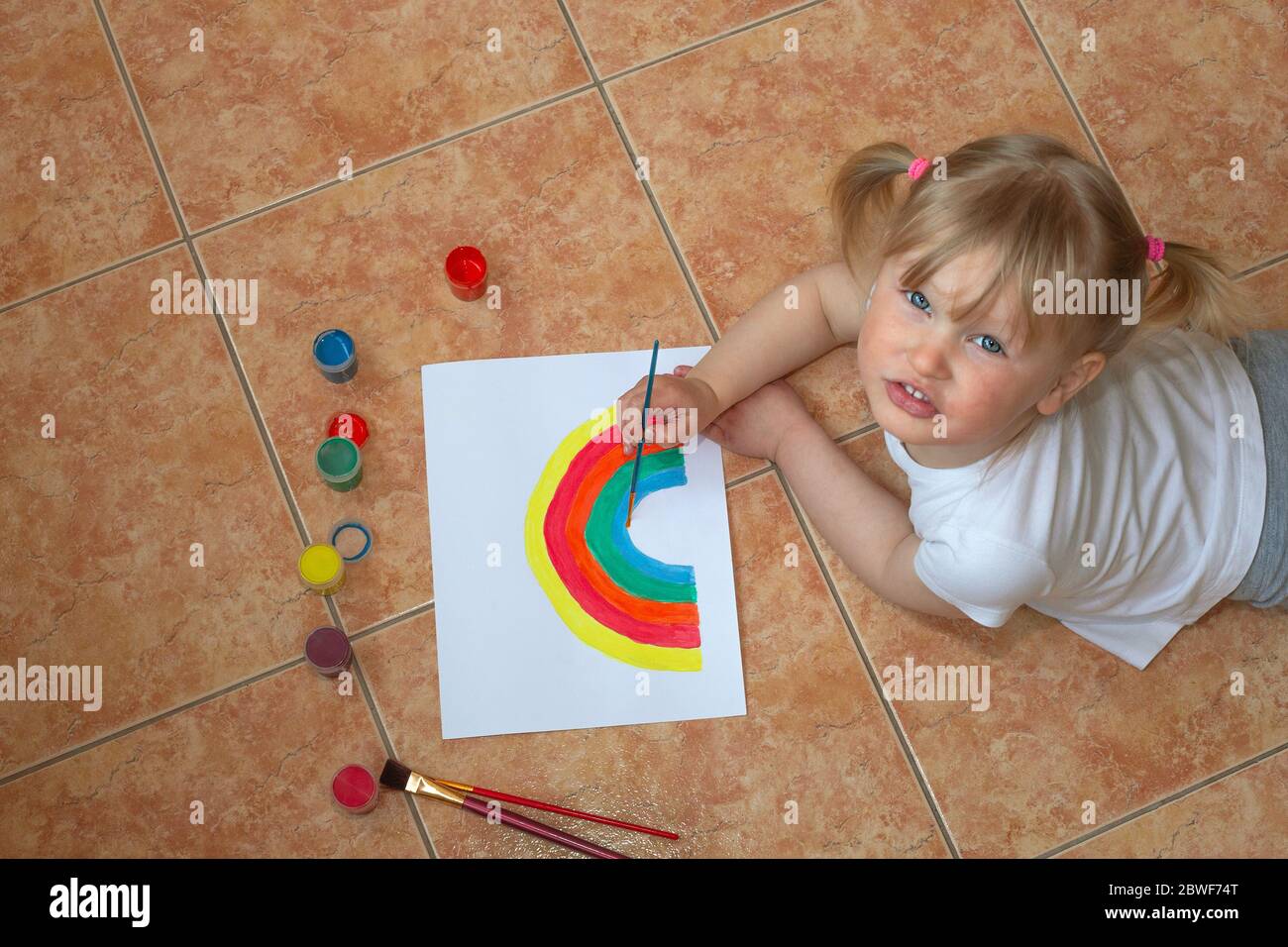 Bambina che disegnava arcobaleno. Segno di speranza durante l'epidemia di coronavirus. Divertimento di quarantena. Arte e artigianato per bambini. Vernice bambini. Scuola capretto che fa l'arte a casa Foto Stock