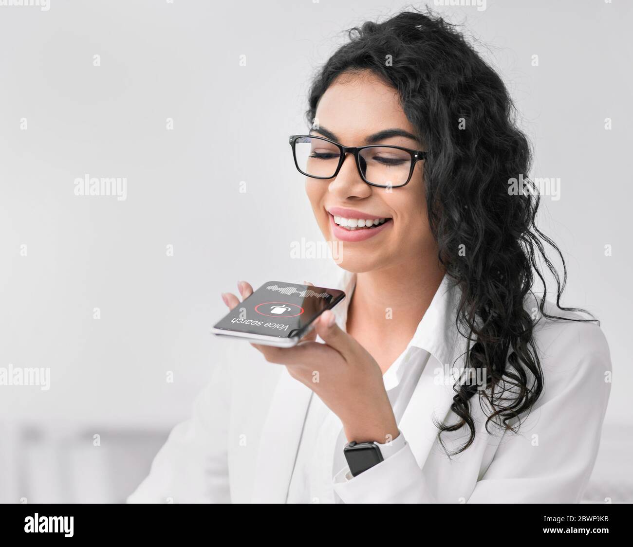 Donna messicana che utilizza l'app di ricerca vocale per smartphone presso Workplace Indoor Foto Stock