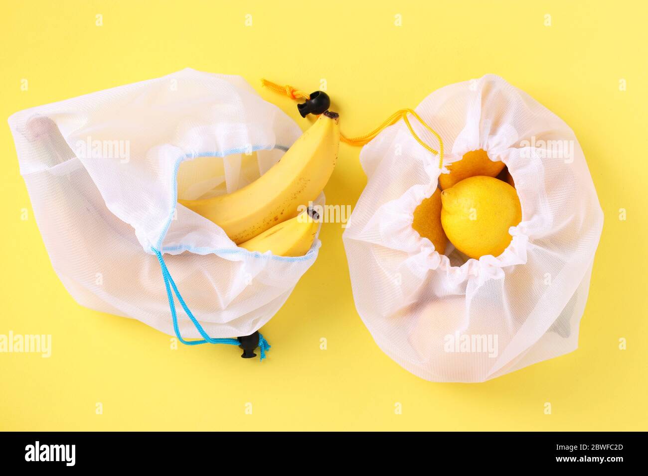 Banane e limoni in sacchetti riutilizzabili eco-friendly mesh su fondo giallo brillante. Concetto di zero rifiuti, arresto inquinamento, Closeup Foto Stock