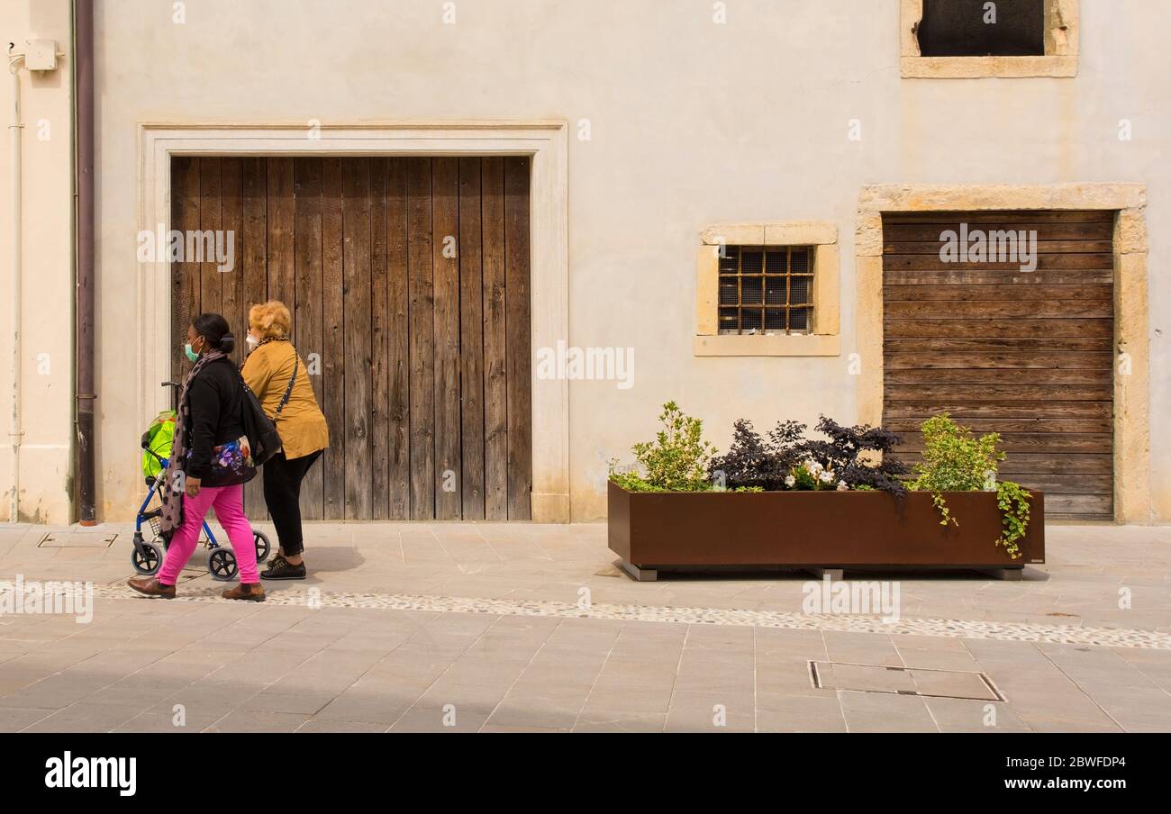 Spilimbergo, Italia - Maggio 31 2020. Una donna anziana che indossa una maschera facciale è accompagnata attraverso il centro storico di Spilimbergo, nella provincia di Udine Foto Stock