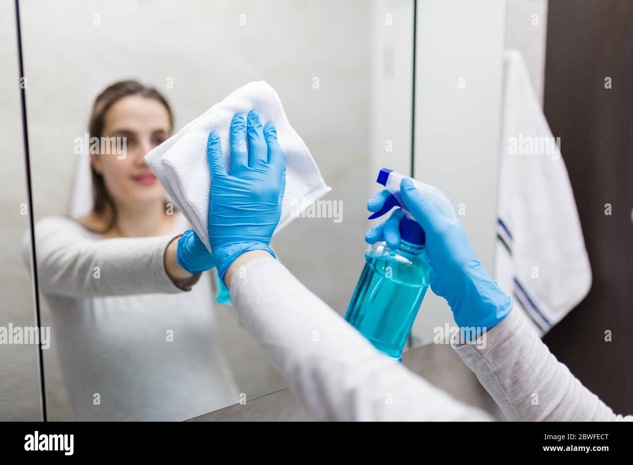 Specchio per lucidatura giovane donna con straccio e disinfettante spray. Servizio di pulizia e pulizia. Foto Stock