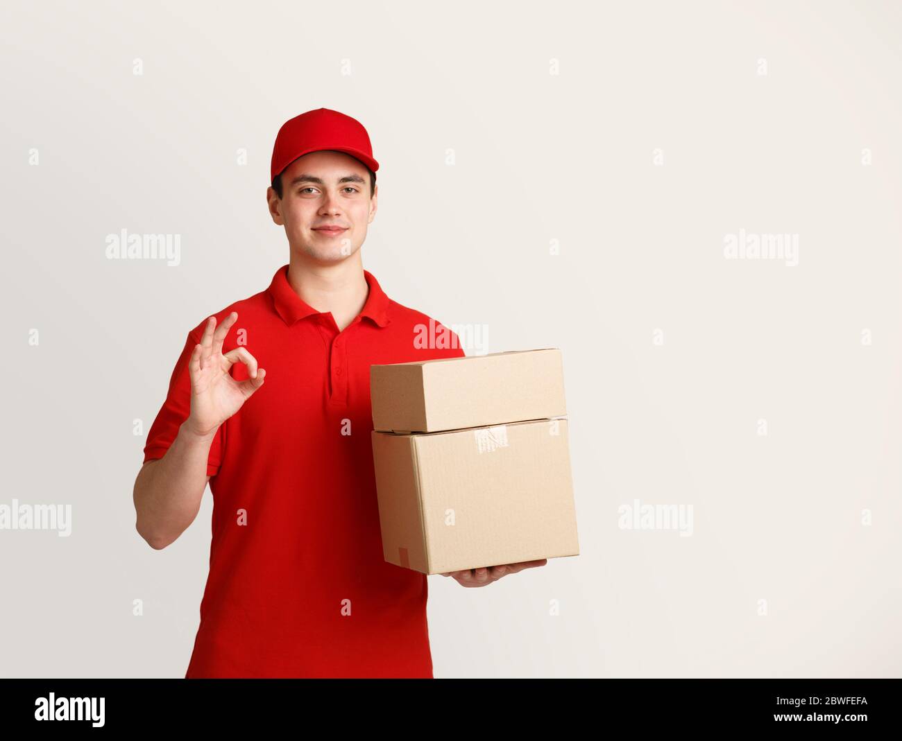 Il corriere amichevole contiene scatole di cartone e mostra un gesto ok Foto Stock