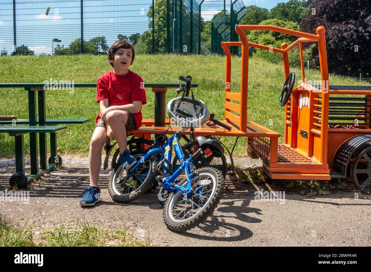 Un ragazzo si siede su una panchina in un parco per riposarsi. Ha la sua bicicletta con lui. È una calda giornata estiva. Foto Stock