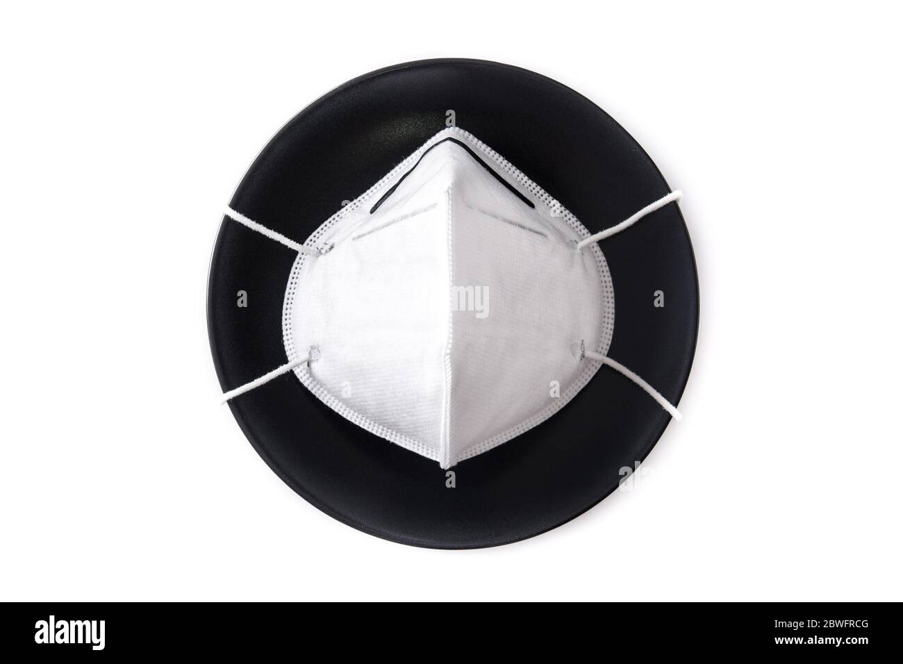 Maschera protettiva su piastra nera, forchetta e coltello. Mangiare in un ristorante durante un concetto pandemico di coronavirus. Foto Stock