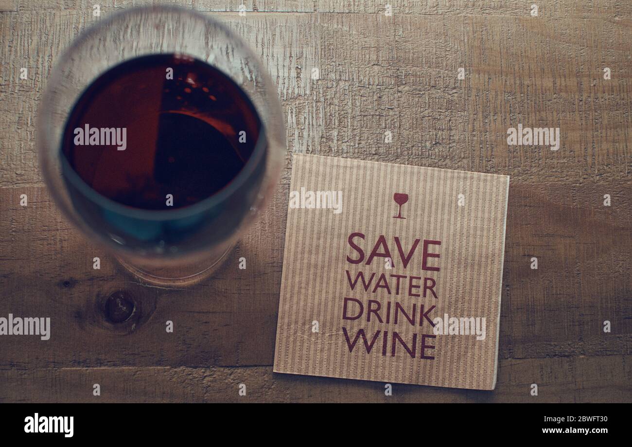 Vista dall'alto di un bicchiere di vino rosso e di un tovagliolo di carta con il testo "Salva acqua, vino da bere" su sfondo di legno. Foto Stock