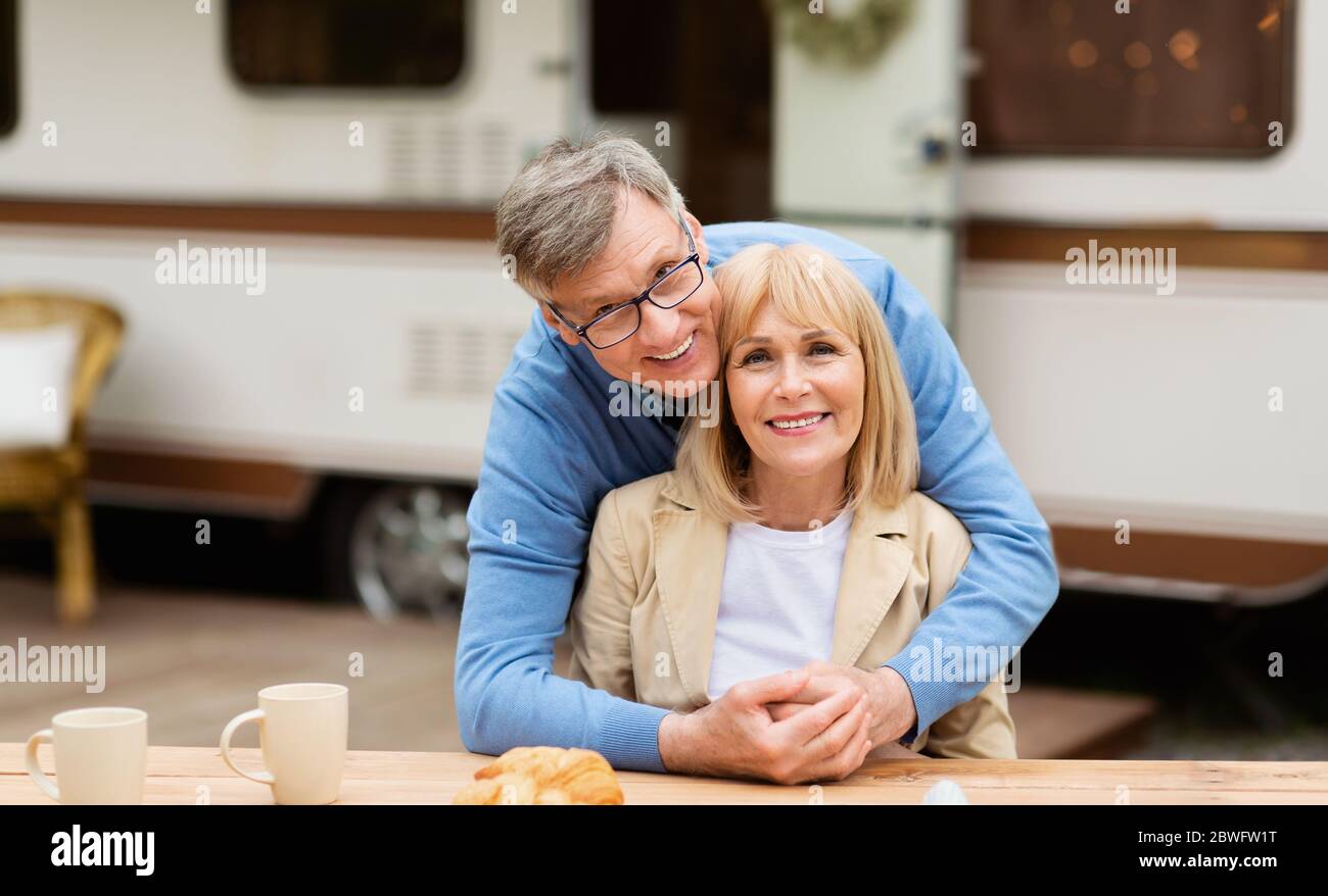 Uomo maturo sorridente che abbracciava la sua bella moglie davanti al veicolo da campeggio all'aperto Foto Stock