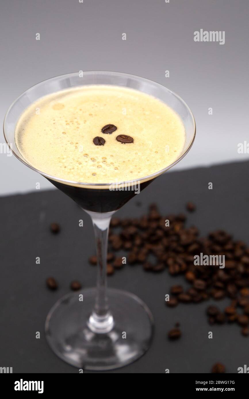 Un espresso Martini servito in un bicchiere martini e guarnito con chicchi di caffè arrosto. Il bicchiere è visibile con chicchi di caffè appena tostati. Foto Stock