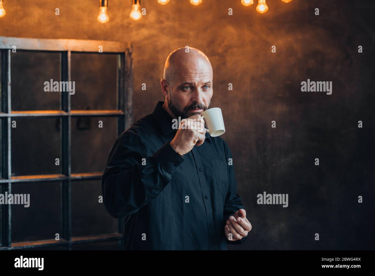 triste uomo di mezza età serio vestito con una camicia nera pensa ai suoi problemi in una stanza con pareti scure Foto Stock