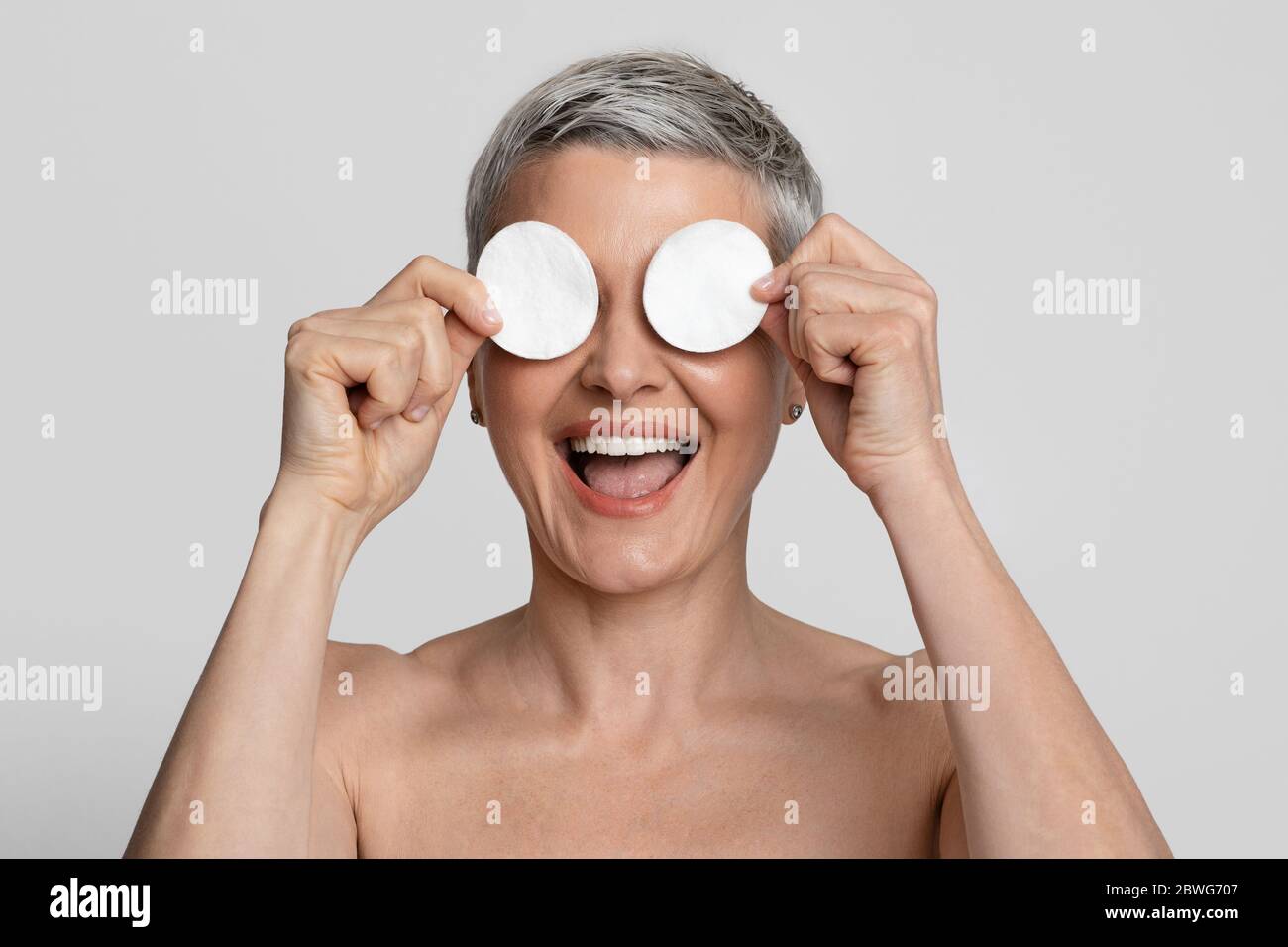 Divertimento per la pelle. Donna matura positiva che copre gli occhi con tamponi in cotone e Laughing Foto Stock