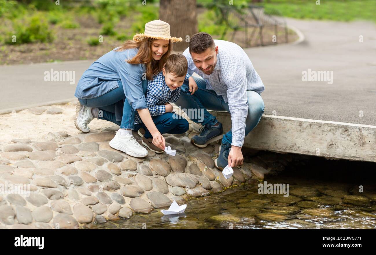 Adorabile ragazzino e i suoi genitori che giocano con barche di carta in un piccolo fiume al parco Foto Stock