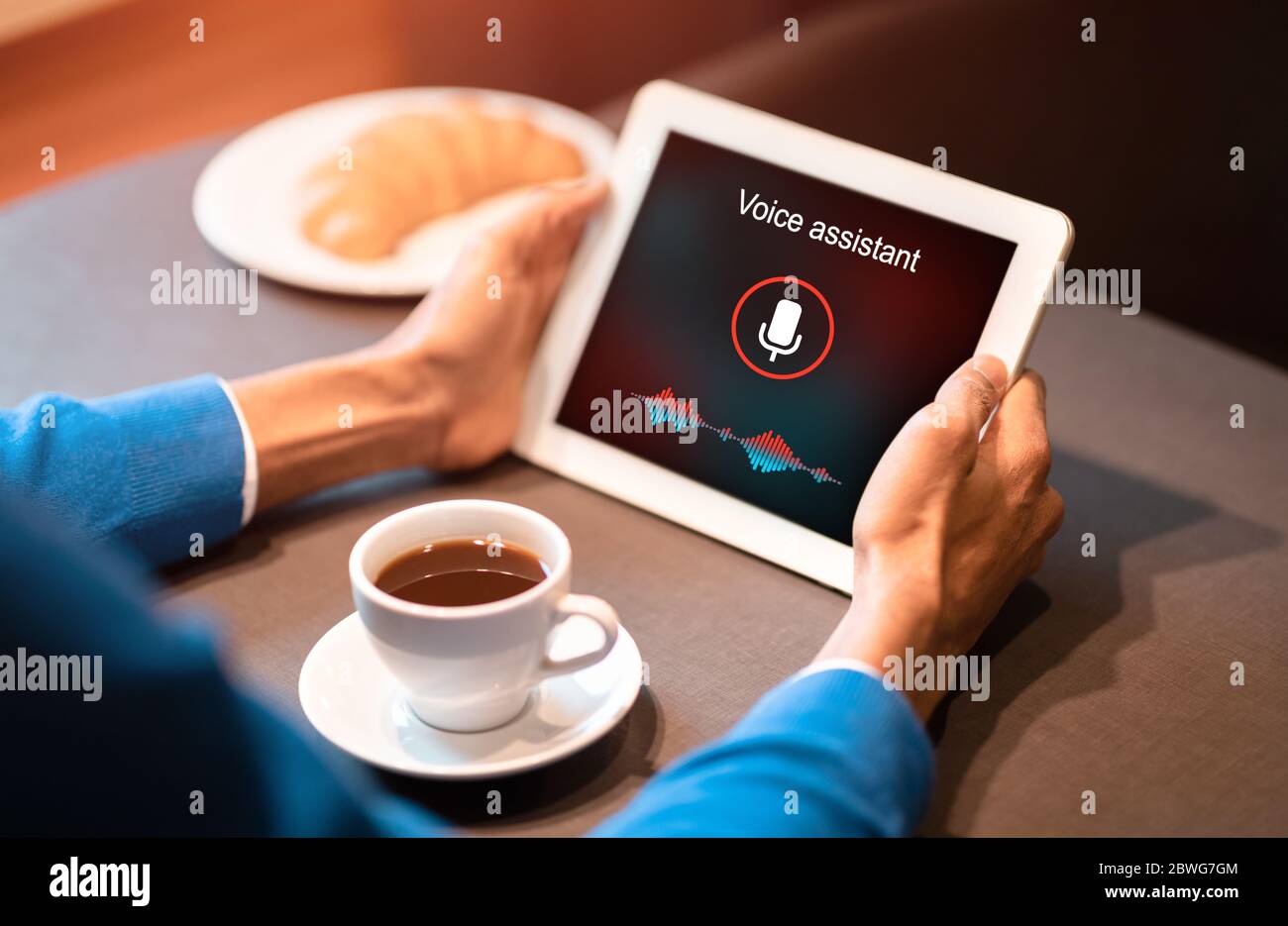 Man Holding Tablet utilizzando Voice Assistant seduto in caffè, ritagliato Foto Stock
