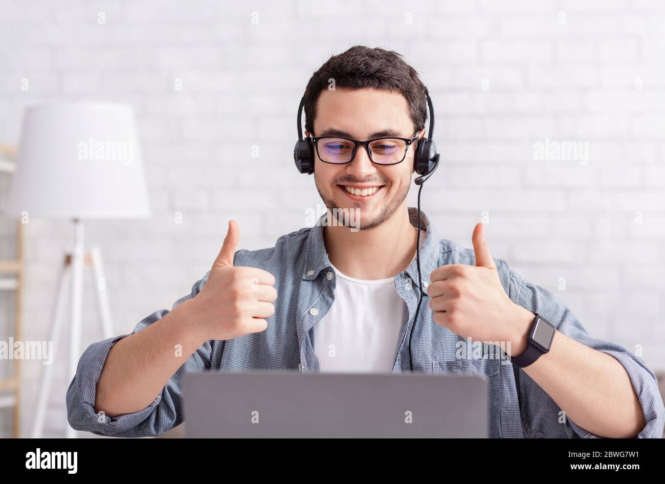 Lavoro online. Il ragazzo sorridente con la cuffia mostra un segno eccellente con la mano Foto Stock