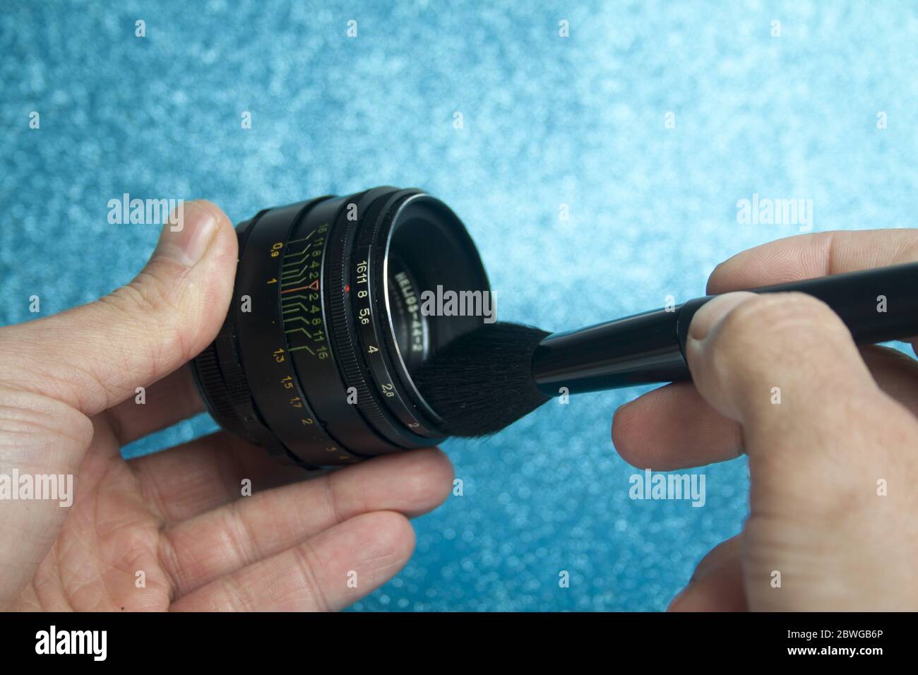 Mani che tengono una spazzola cosmetica e la puliscono con una vecchia lente manuale su sfondo blu. Foto Stock