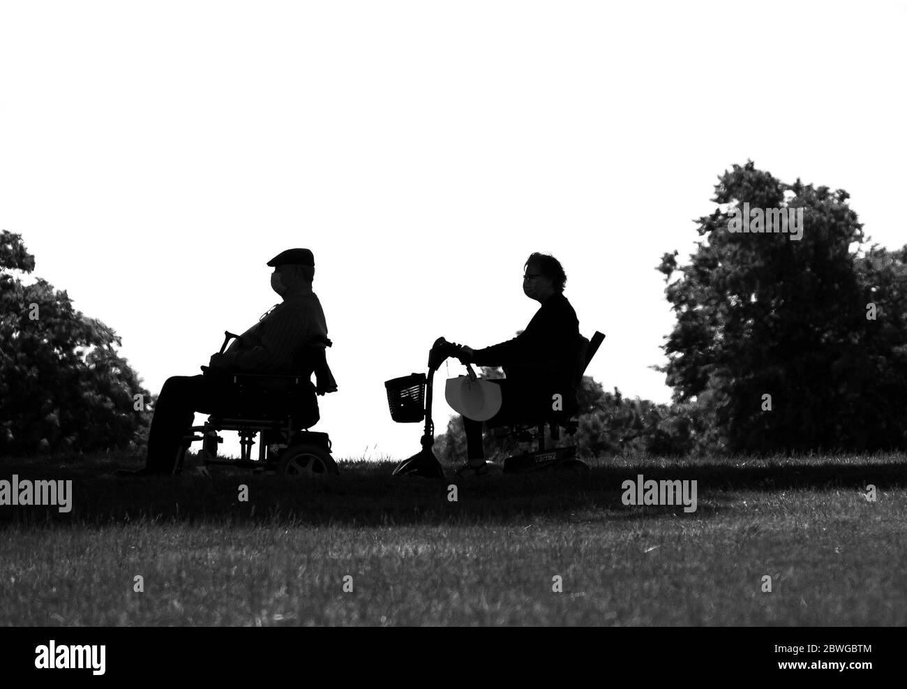 Due anziani in scooter di mobilità che osservano le distanze sociali Foto Stock
