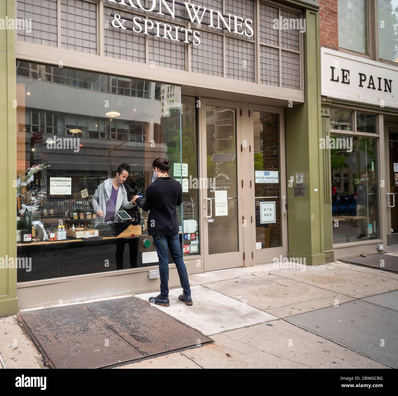 Un cliente in un negozio di vini e liquori a New York utilizza la sua carta tramite il chip RFID per il pagamento senza contatto attraverso la vetrata, sabato 23 maggio 2020. (© Richard B. Levine) Foto Stock