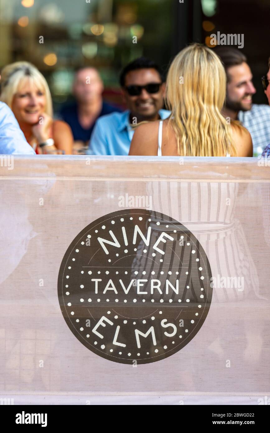 Un gruppo di amici etnicamente diversi si siedono e bevono bevande al sole estivo serale a Nine Elms vicino alla centrale elettrica di Battersea Foto Stock