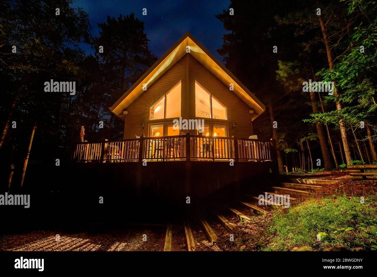Casa vacanza con finestre illuminate nel bosco. Idilliaca cabina o cottage fotografato di notte. I concetti potrebbero includere viaggio, natura, arco, ecc. Foto Stock