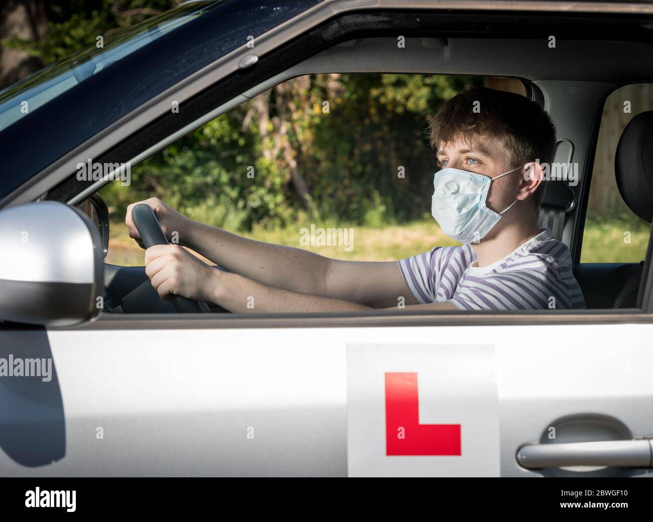 Teenage allievo driver un indossare una maschera a causa della pandemia del coronavirus in attesa di iniziare la sua lezione di guida. Foto Stock