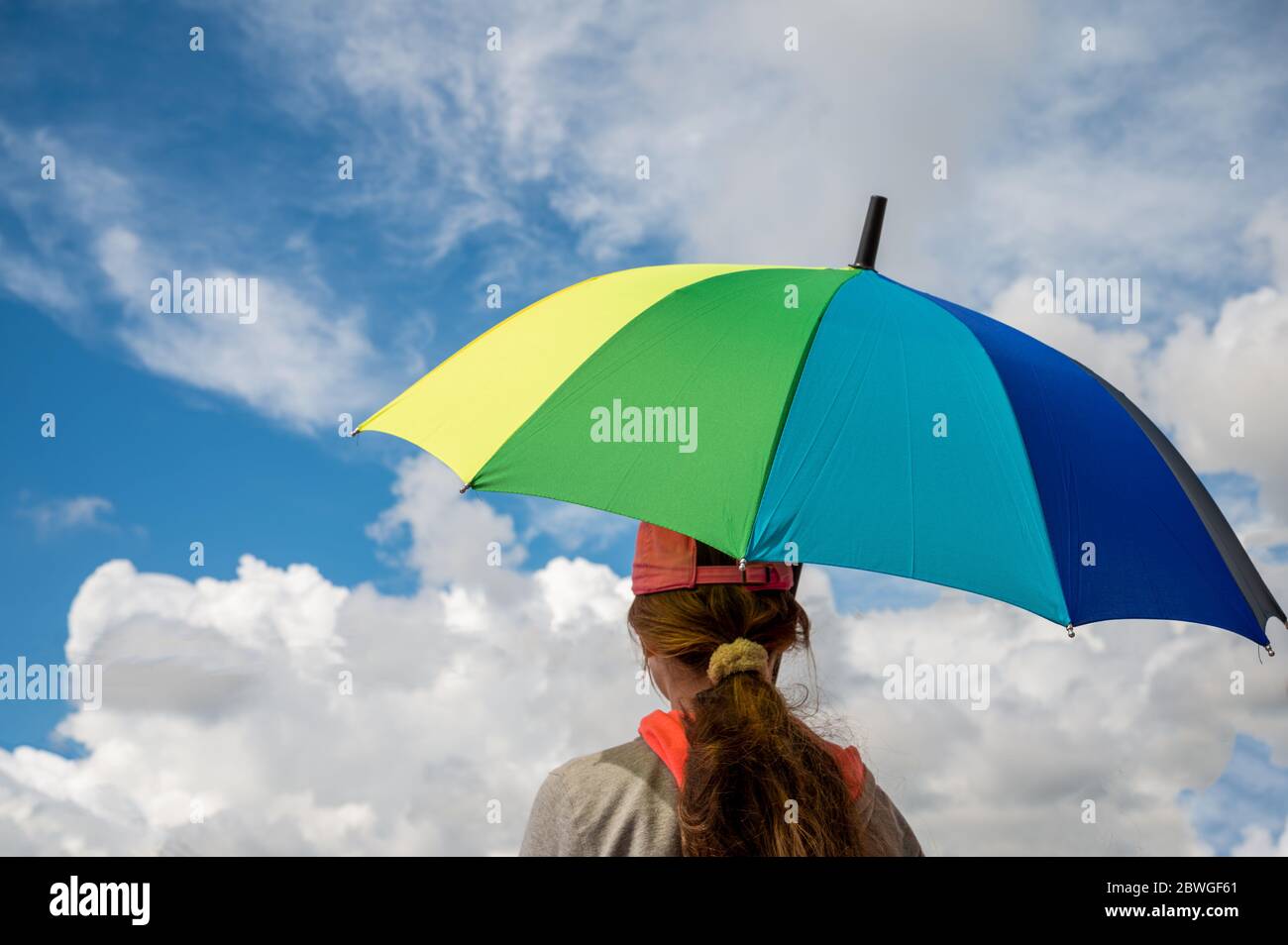 Ragazza giovane che tiene un ombrello arcobaleno colorato sotto un cielo nuvoloso Foto Stock