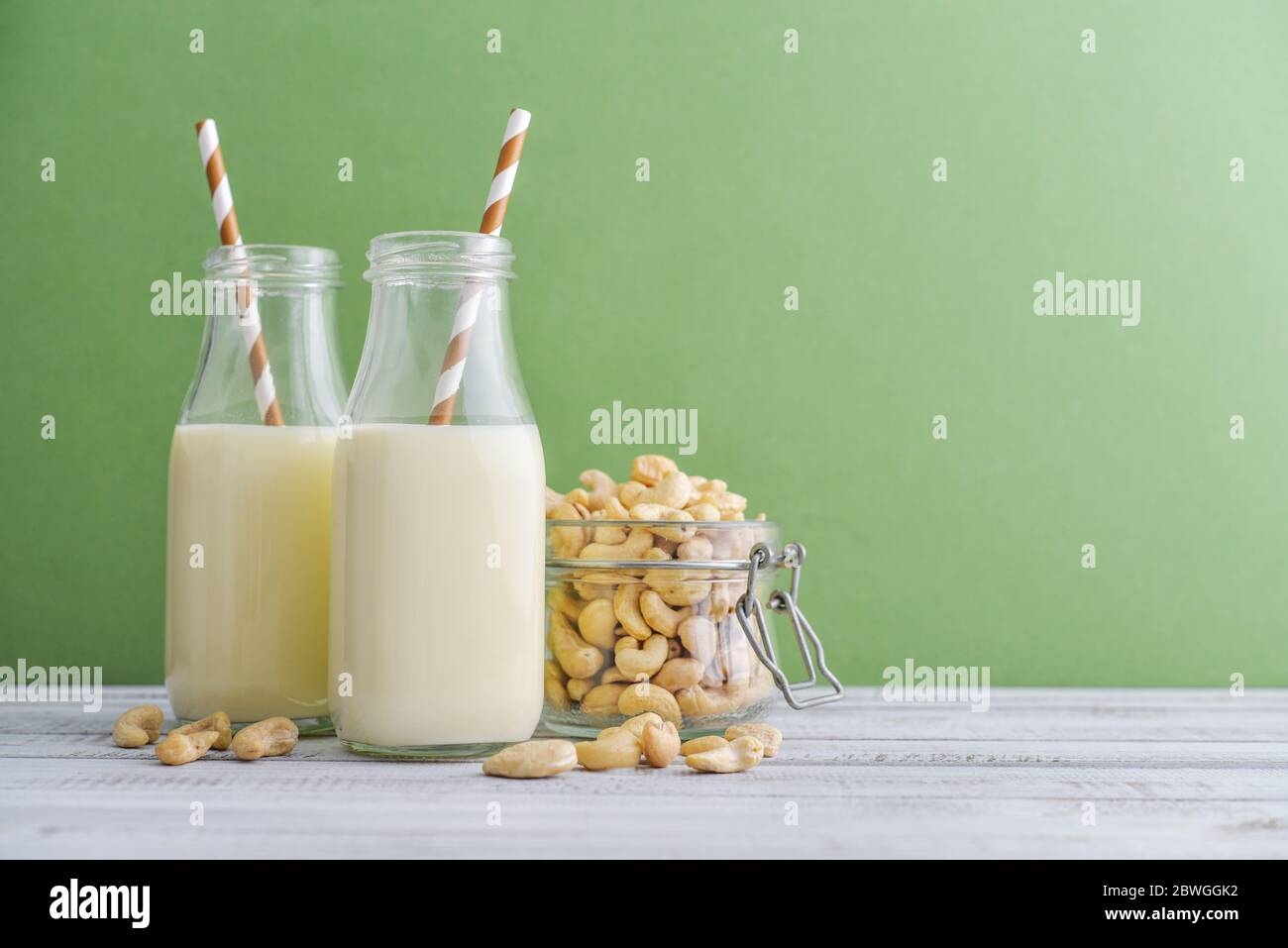 Due bottiglie di latte di anacardi vegetariano con noci di anacardi su sfondo verde Foto Stock