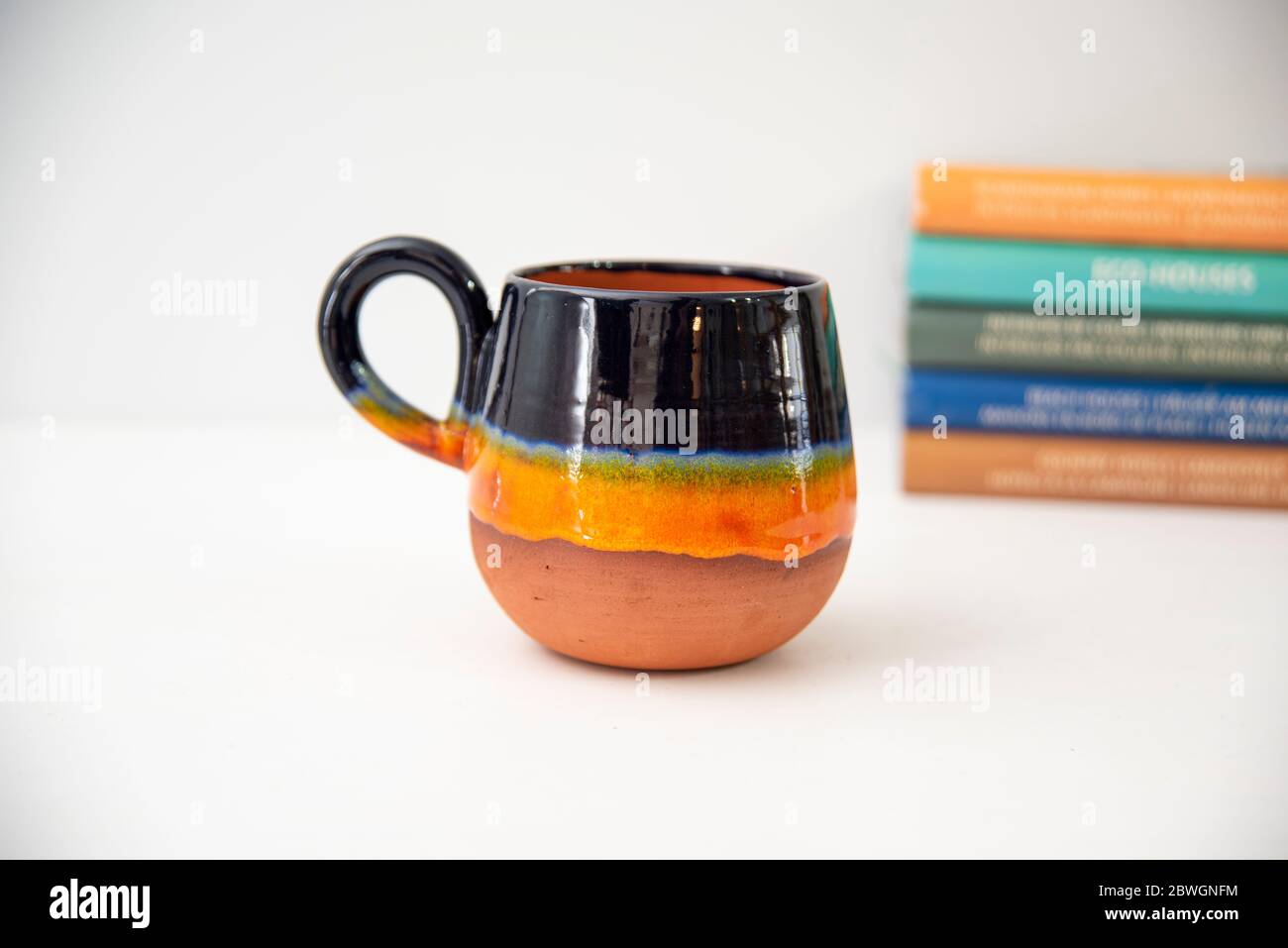 tazza da caffè in ceramica colorata fatta a mano con libri sul tavolo Foto Stock