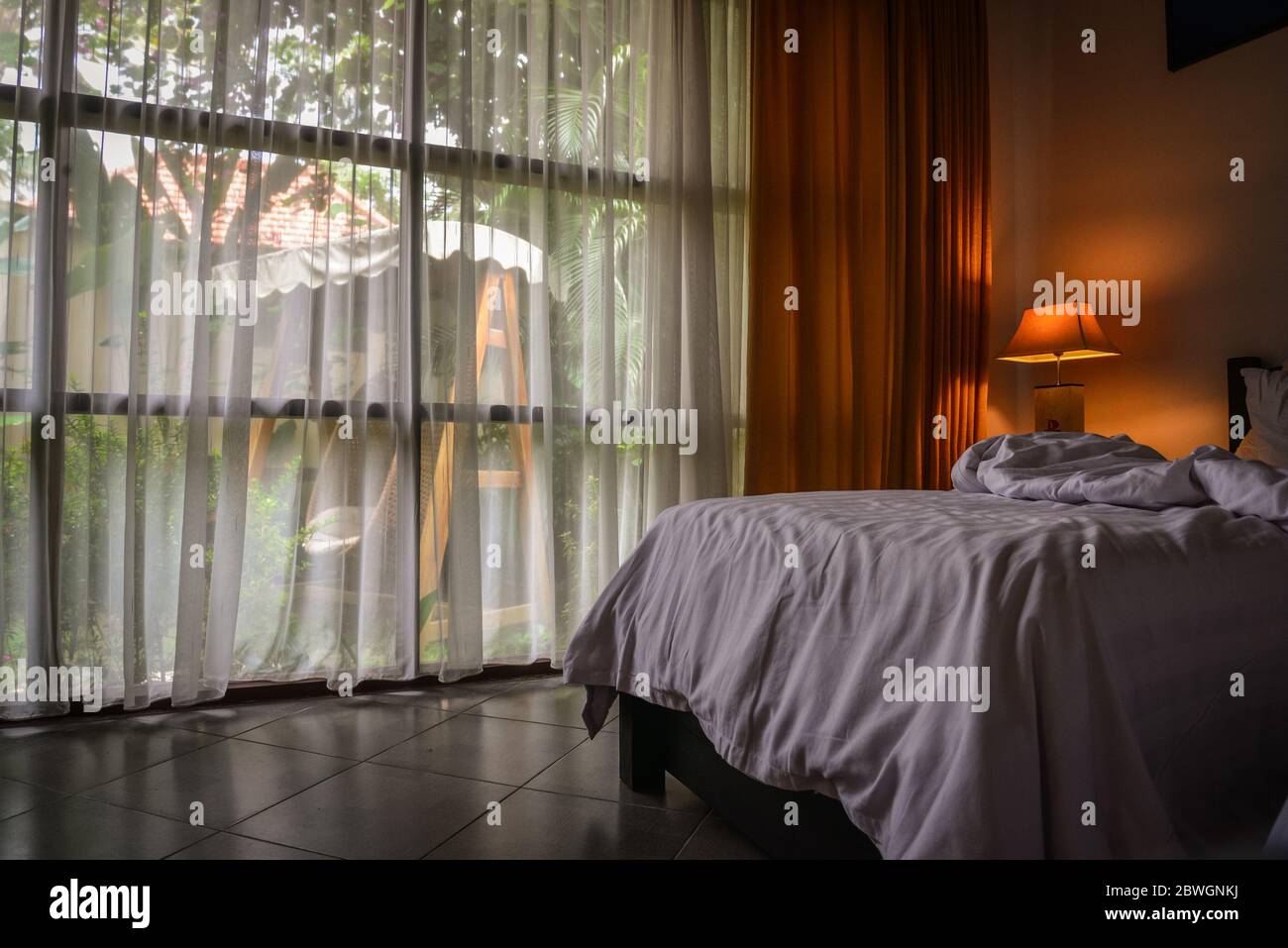 BALI, INDONESIA - 14 GENNAIO 2018: Camera d'albergo con letto e sedie in vimini appesi fuori dalla finestra in territorio Discovery Candidasa Cottages e VI Foto Stock