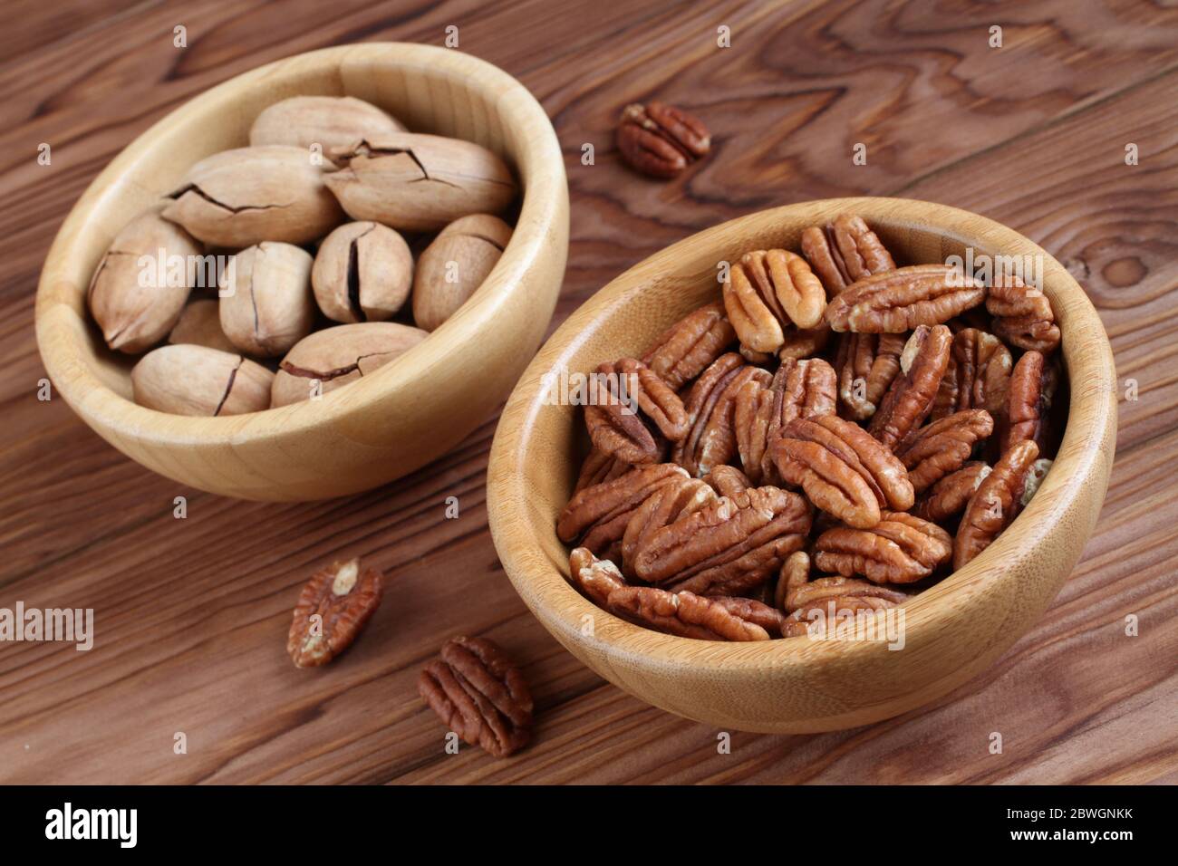 Noci pecan pelate e noci pecan non pelate in ciotole di bambù su sfondo di legno Foto Stock