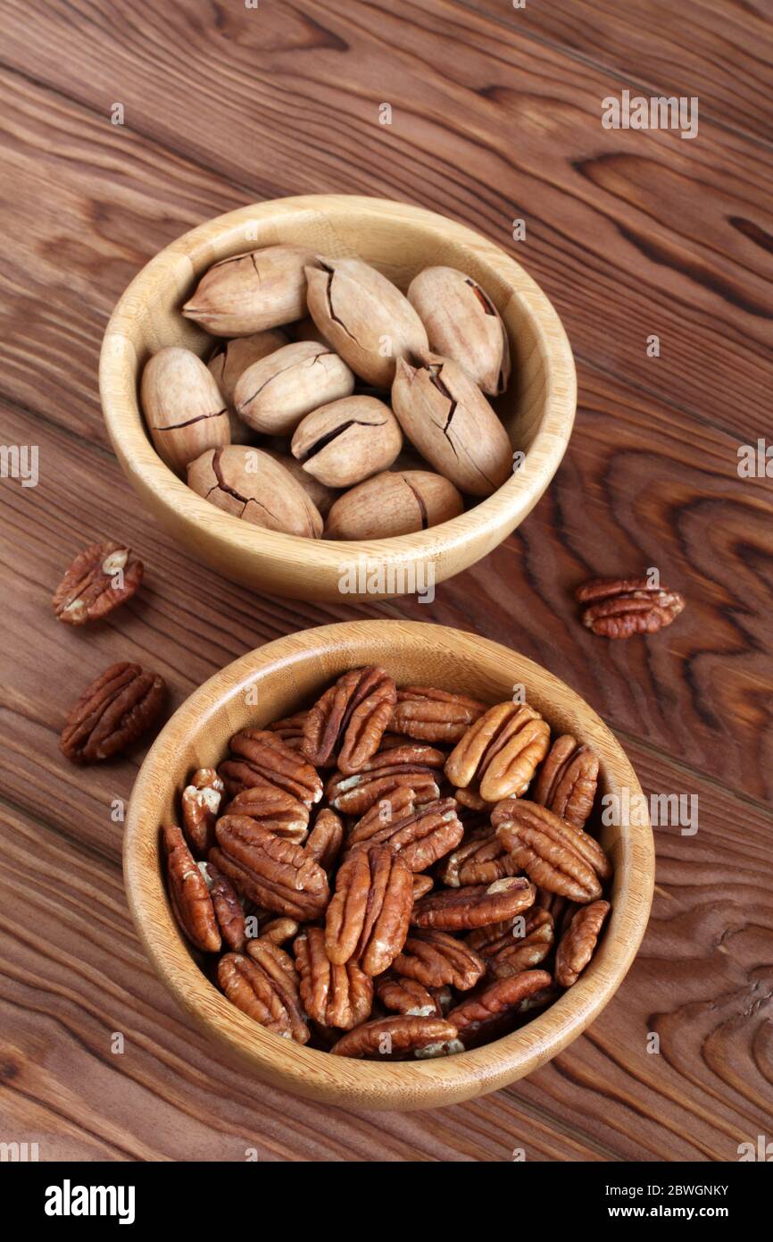 Noci pecan pelate e noci pecan non pelate in ciotole di bambù su sfondo di legno Foto Stock