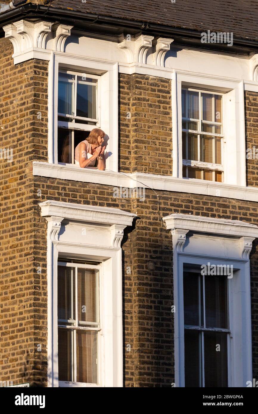 Una donna solista si batte per gli accompagnatori dalla sua finestra su Stockwell Road, su quello che è stato assegnato come evento finale, durante il blocco COVID-19 di Londra, il 28 maggio Foto Stock