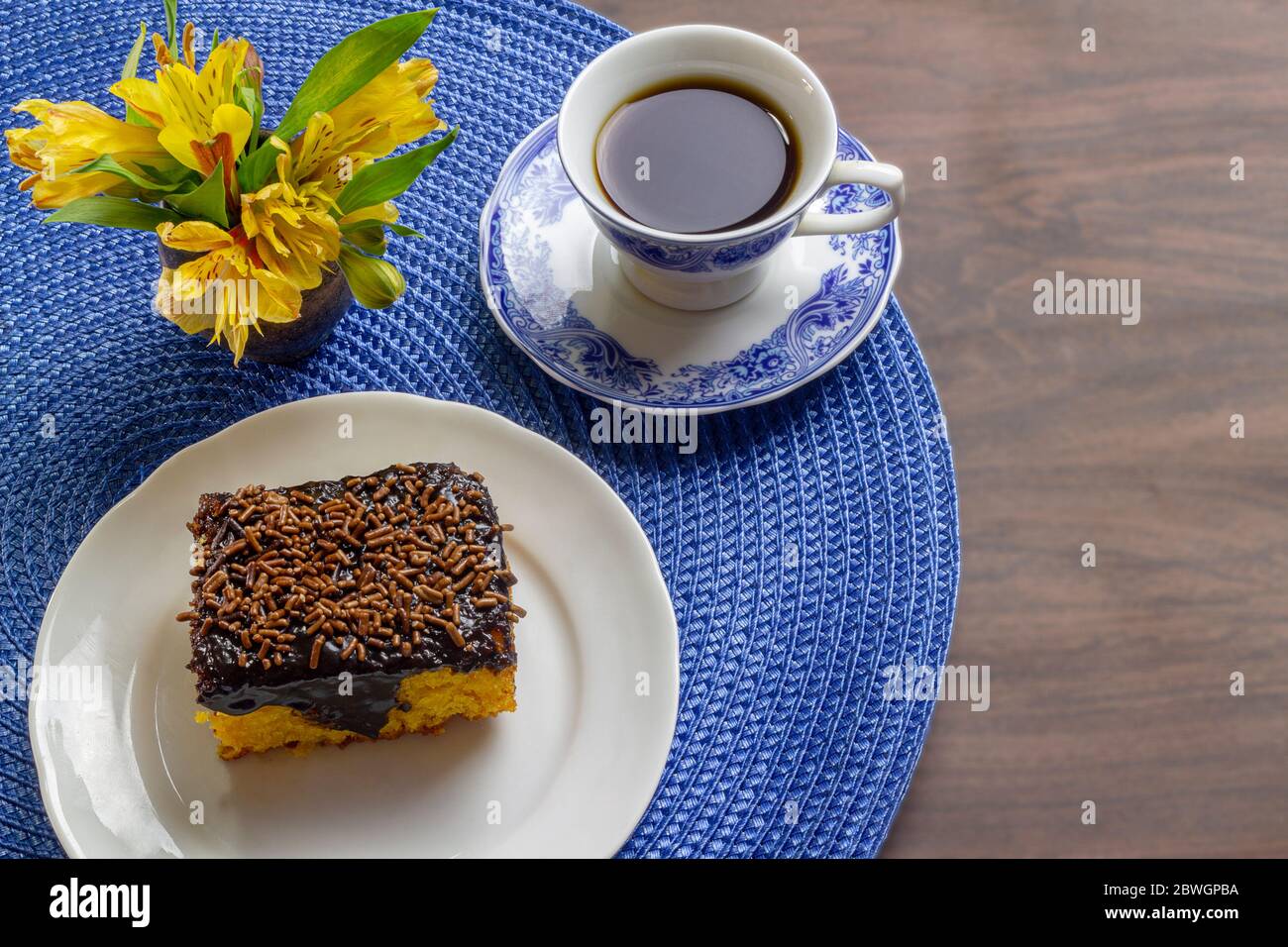 Torta di carote con glassa di cioccolato e tazza di caffè su tavolo di legno decorato con un fiore giallo. Foto Stock