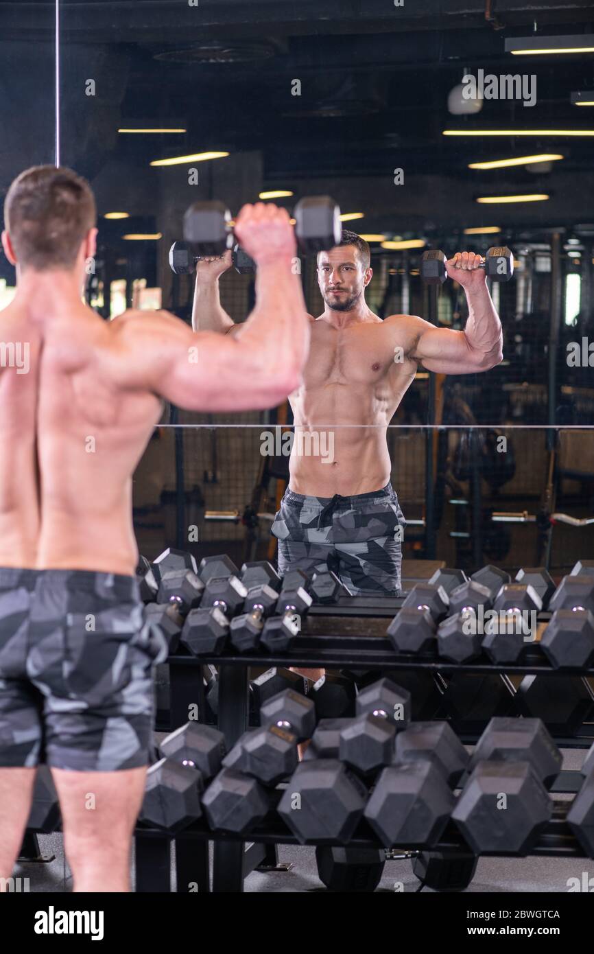 Uomo muscoloso sexy facendo le spalle esercizio e guardando lo specchio Foto Stock