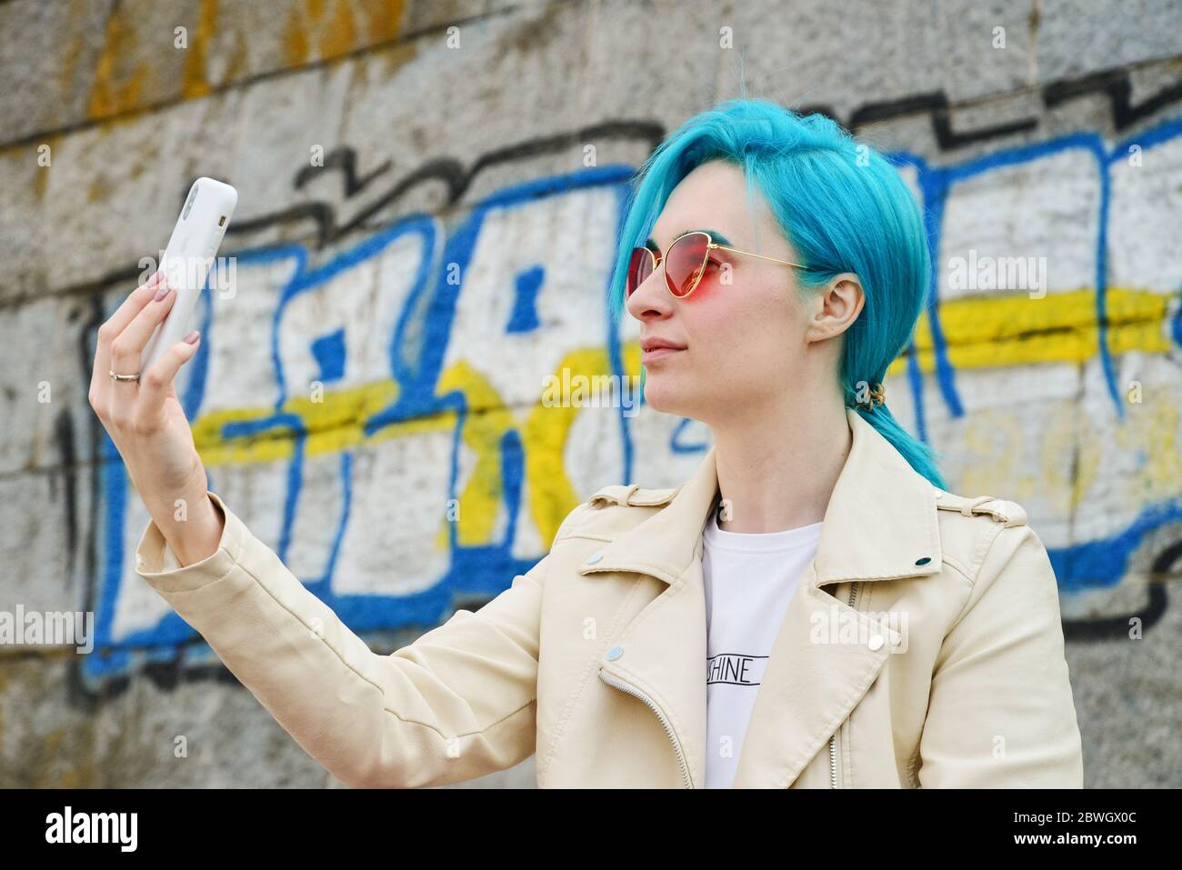 Kiev, Ucraina - 22 aprile 2019: Bella giovane ragazza caucasica con capelli blu utilizza iPhone XS per selfie all'aperto Foto Stock