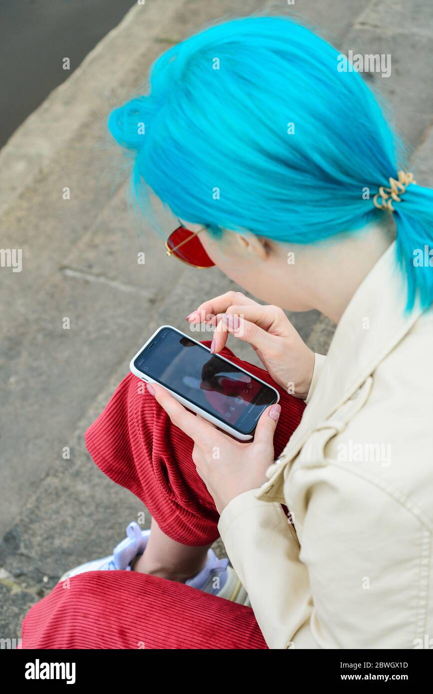 Kiev, Ucraina - 22 aprile 2019: Bella giovane ragazza caucasica con capelli blu utilizza iPhone XS all'aperto Foto Stock