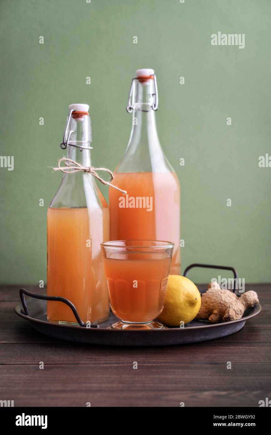 Tè Kombucha crudo fermentato in casa in vetro e bottiglia con limone e zenzero su sfondo verde Foto Stock