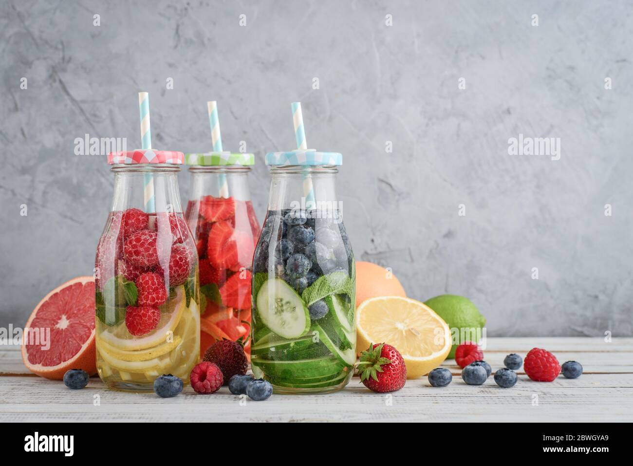Acqua infusa con frutta fresca, verdure e bacca in bottiglie su sfondo grigio Foto Stock