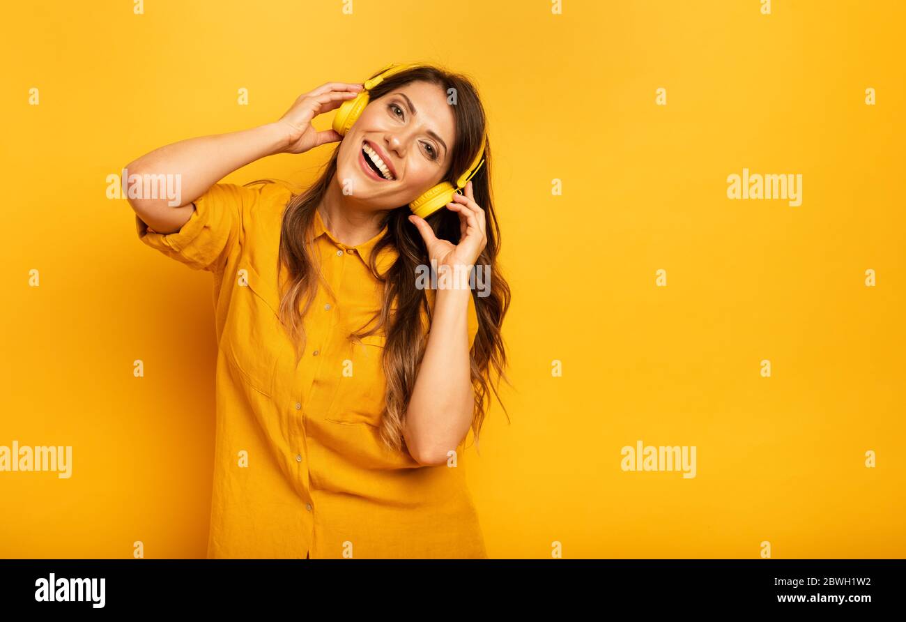 Ragazza con auricolare giallo ascolta musica e danze. emozionale e espressione energica Foto Stock