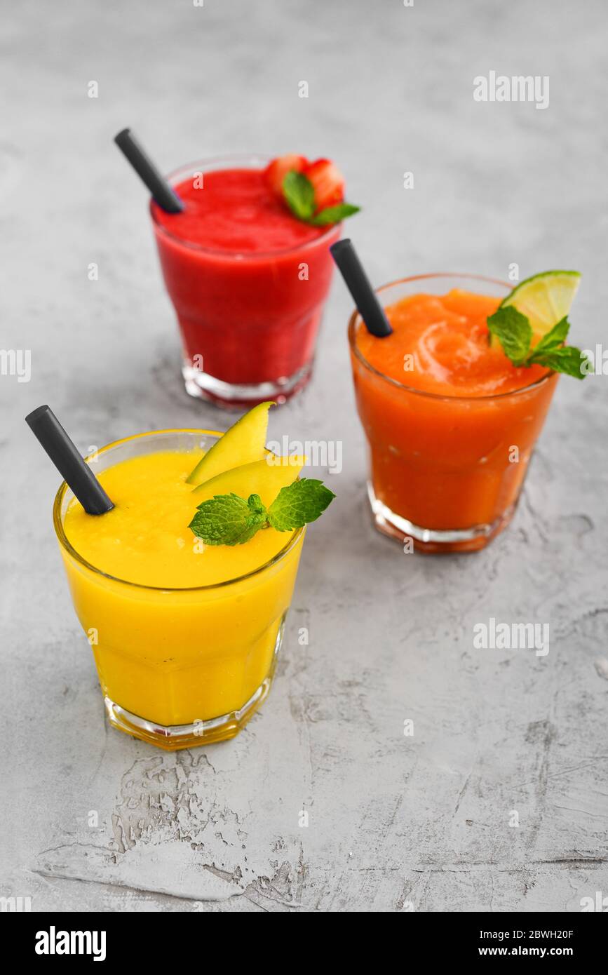 Frullati freschi di fragola, mango e papaia in bicchieri su sfondo grigio. Foto Stock