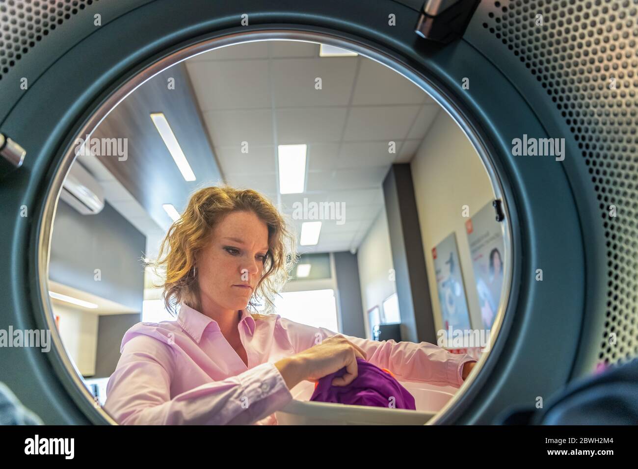 donna che mette i vestiti in un asciugatore in una lavanderia pubblica Foto Stock