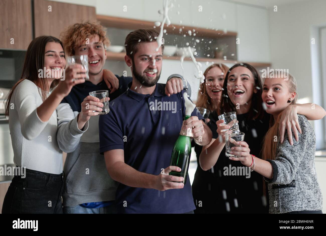 Allegri giovani amici che aprono una bottiglia di champagne Foto Stock
