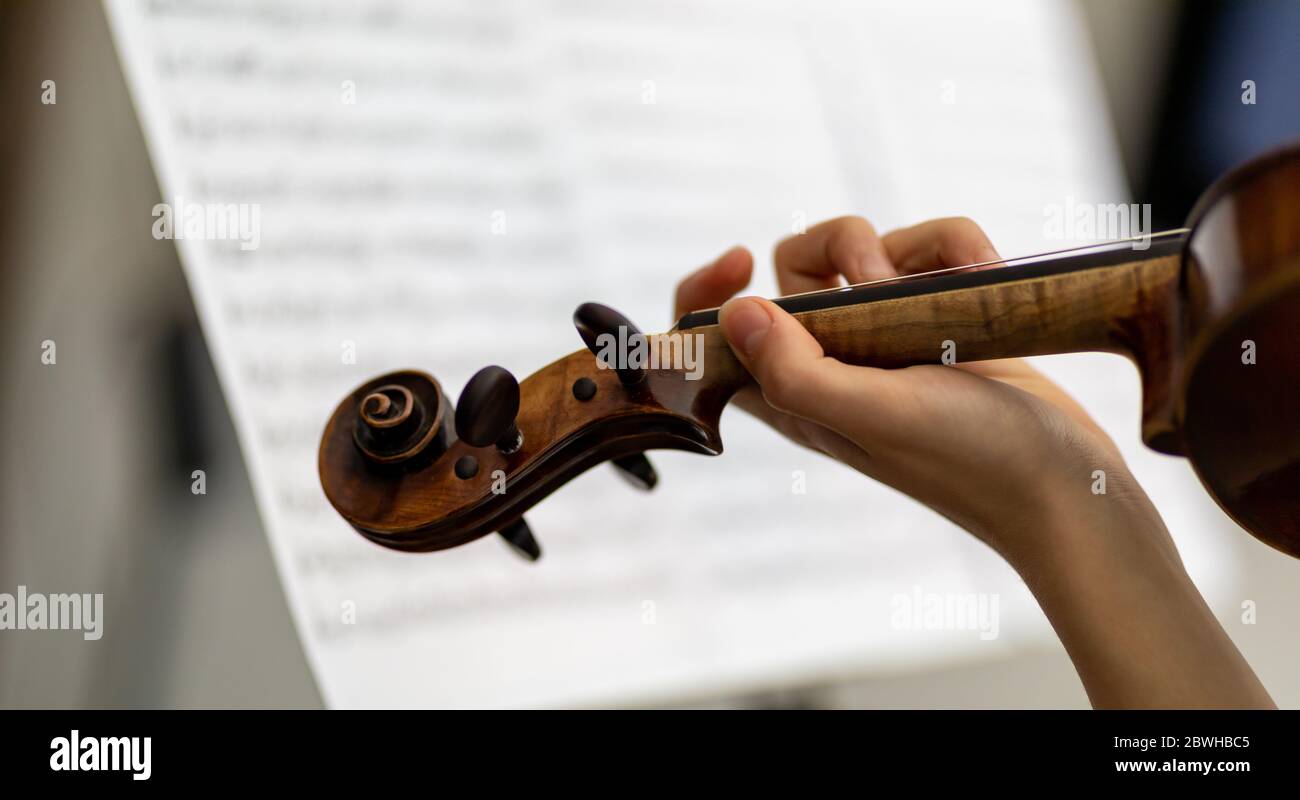 Donna violinista che suona un antico violino barocco in un primo piano sopra la vista della spalla della sua mano sulle corde contro uno sfondo di una musica spartito Foto Stock