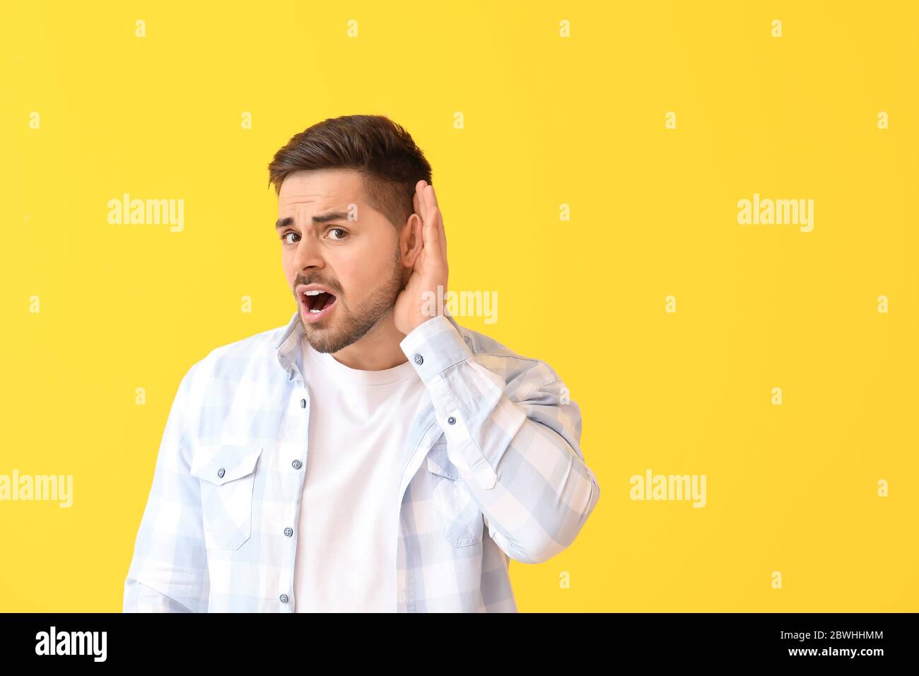 Giovane uomo che cerca di sentire qualcosa su sfondo a colori Foto Stock