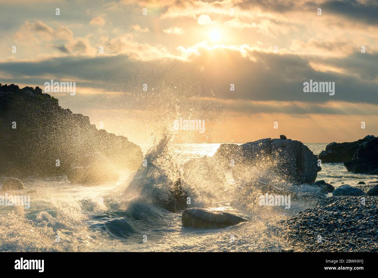 Big Wave ha colpito la roccia in spiaggia, acqua di mare splash fino al cielo con il sole. Tramonto tramonto tramonto al mare. Tempesta. Stagcape. Foto Stock