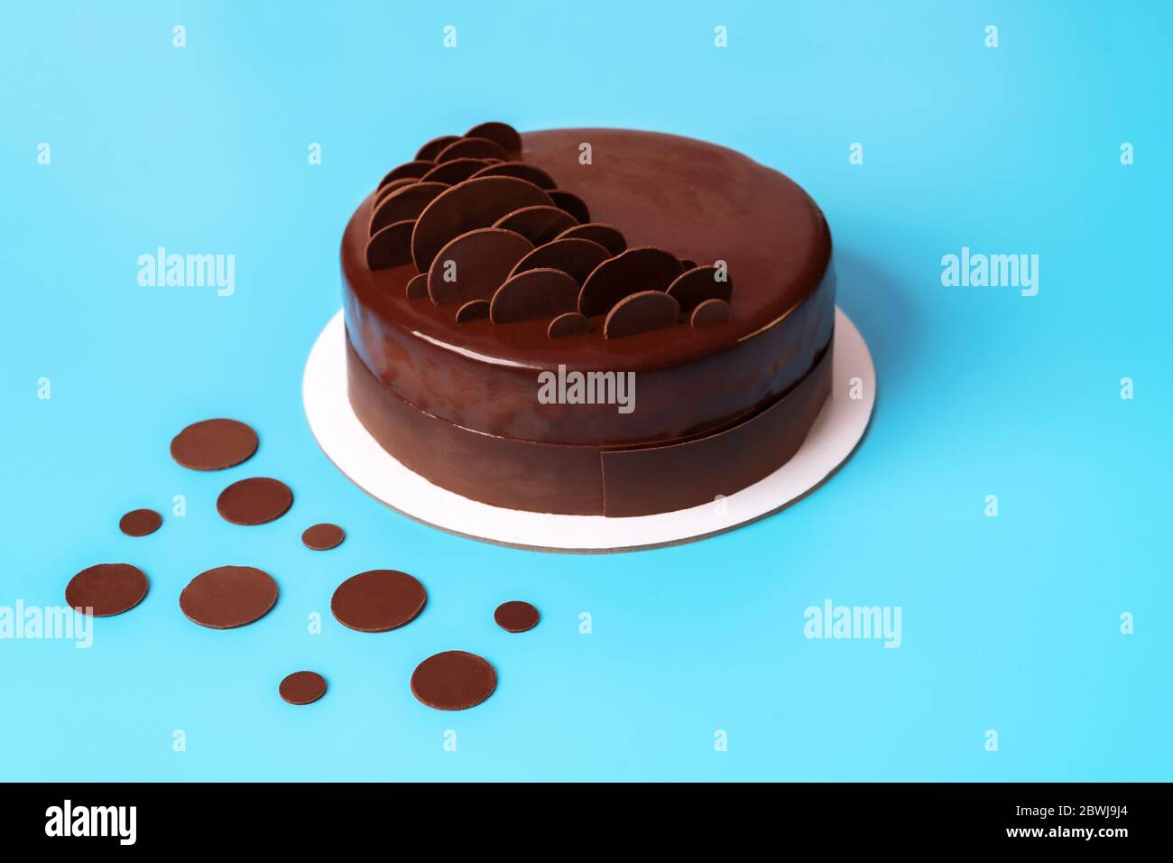 Torta di mousse al cioccolato fondente ricoperta di glassa a specchio e decorata con gocce di cioccolato rotonde su sfondo blu. Torta moderna ed elegante. Primo piano. Copia Foto Stock